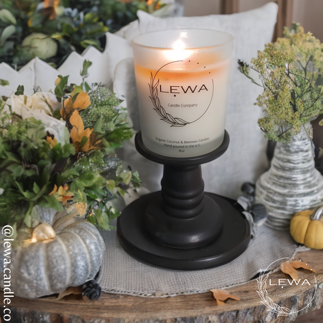 LEWA Autumn Glow candle burning on a black candle holder surrounded by autumn decorations, decorative plants, and warm seasonal accents